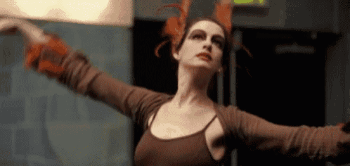 a woman in a brown top is dancing with her arms outstretched in a room .