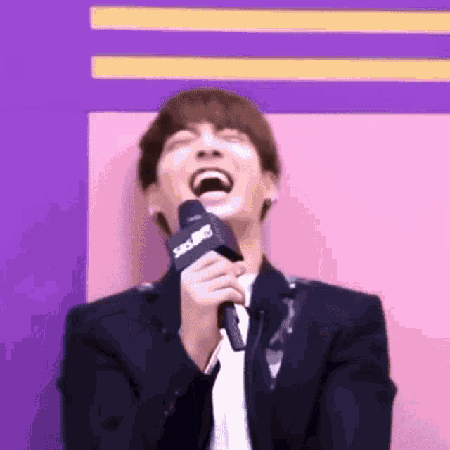 a young man in a suit is laughing while holding a microphone .