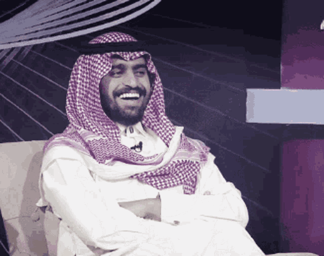 a man with a beard wearing a purple and white checkered scarf is smiling