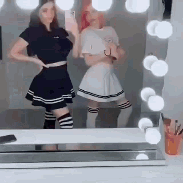 two girls are taking a selfie in front of a mirror in a room .