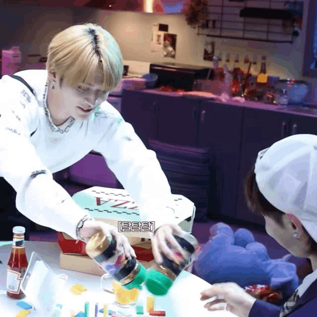 a man in a white shirt is pouring a bottle of ketchup on a table with a pizza box in the background