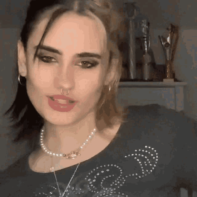 a woman with a nose ring and a pearl necklace is wearing a black shirt .