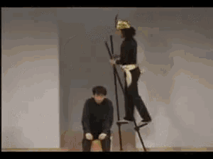 a woman is standing on stilts next to a man kneeling down