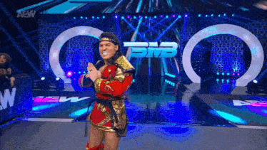 a wrestler in a red and gold outfit is standing on a stage with a aew logo in the background
