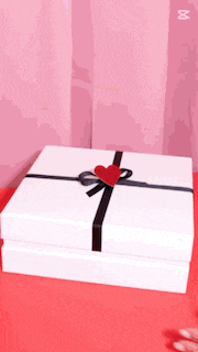 a white box with a black ribbon and a red heart on it is on a red table .