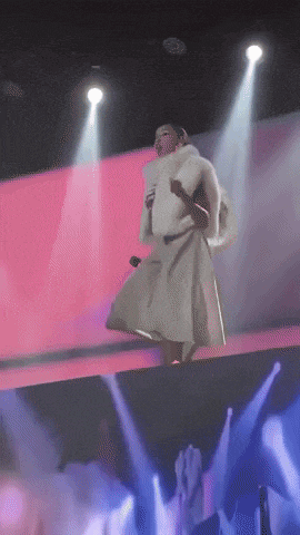 a woman in a white fur coat sings into a microphone on stage