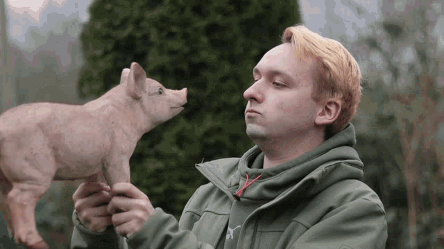 a man in a green jacket is holding a pig