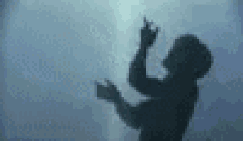 a shadow of a person standing in front of a wall with their hands in the air .
