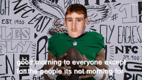 a man in a green nfl jersey holds a football in front of a wall that says eagles