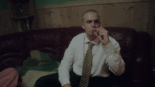a man in a white shirt and yellow tie is smoking a cigarette