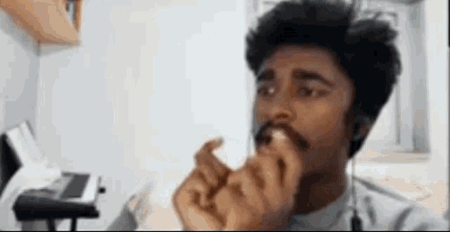 a man with a mustache is eating a piece of food in a room .