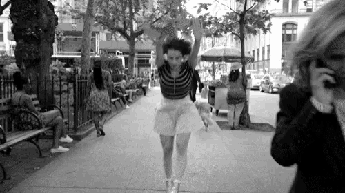 a man is taking a picture of a woman jumping in the air on a sidewalk .