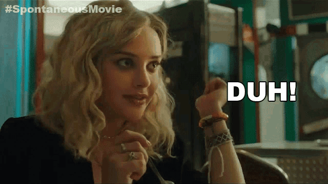 a woman is sitting at a table with the word duh written on her wrist
