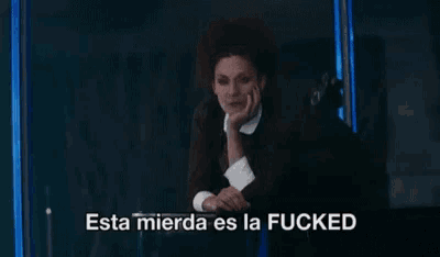 a woman is sitting in front of a window with the words esta mierda es la fucked written on the bottom
