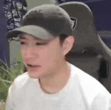 a man wearing a hat and a white shirt is sitting in a chair and making a funny face .