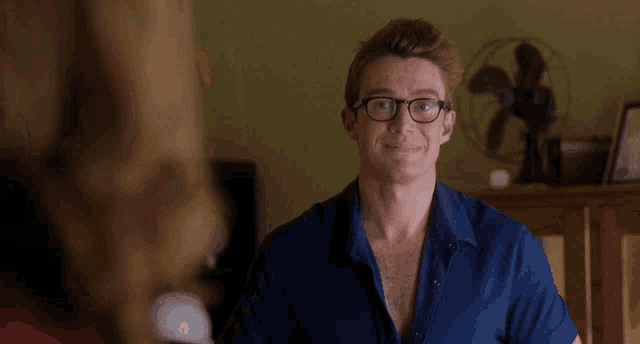 a man wearing glasses is smiling in front of a fan