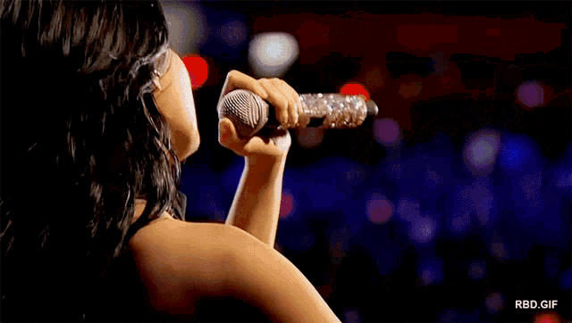 a woman singing into a microphone in front of a crowd with rbd.gif written on the bottom right