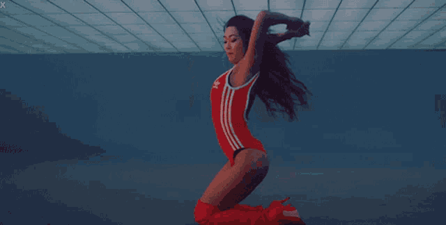 a woman in a red adidas swimsuit is kneeling down in a dark room