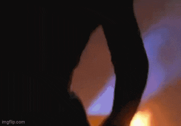 a person in a black hood is standing in front of a fire in the dark .