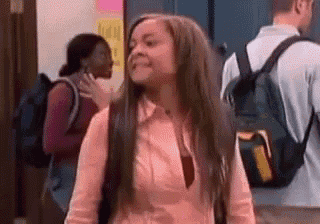 a woman with long hair and a backpack is standing in a hallway with other people .