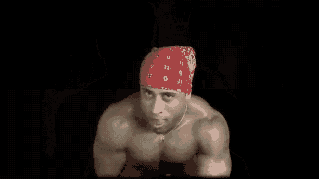 a very muscular man wearing a red bandana and a necklace is giving a thumbs up .