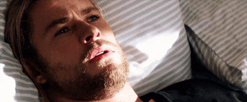 a man with a beard is laying in a bed with striped sheets