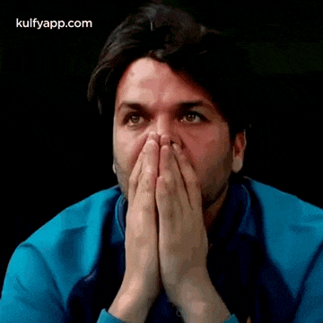 a man is covering his mouth with his hands and looking at the camera .