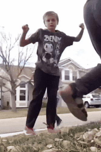 a boy wearing a bendy shirt is standing in the grass
