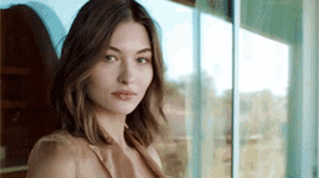 a woman in a brown dress is standing in front of a window .