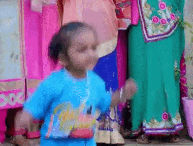 a little girl in a blue shirt is dancing in front of a crowd of people .