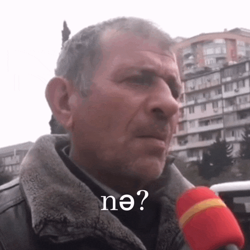 a man is talking into a microphone and the word ne is on the bottom of his face .
