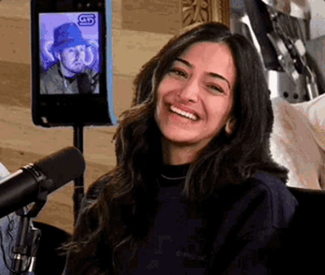 a woman is smiling in front of a microphone while sitting in front of a camera .