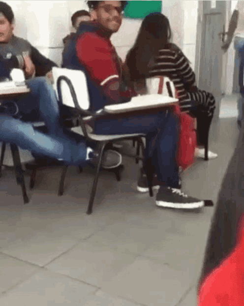 a man sits at a desk with his legs crossed in a classroom