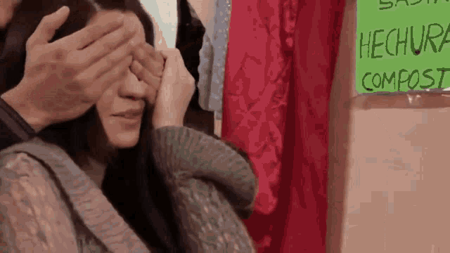 a woman is covering her eyes in front of a sign that says hecho compost