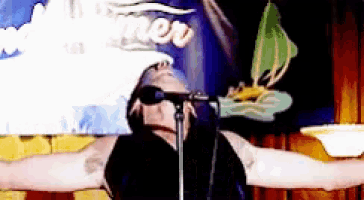a man stands in front of a microphone with his arms outstretched and a sign behind him that says ' new '