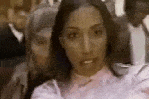 a woman in a pink shirt is taking a selfie with a man in a suit behind her .