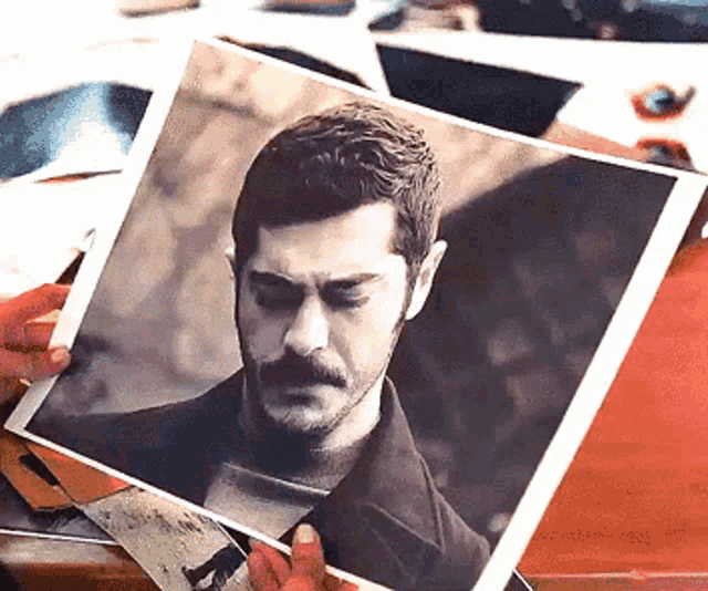 a man with a mustache is holding up a picture of himself