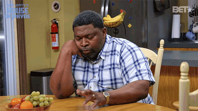 a man sits at a table with a bowl of fruit in front of a refrigerator that says bet on it