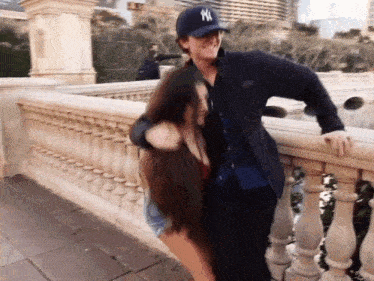 a man wearing a new york yankees hat hugs a woman