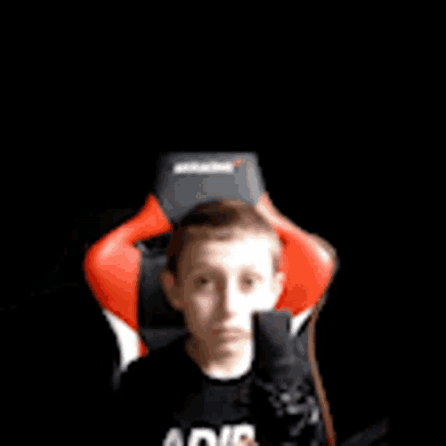 a young boy is sitting in a red and black gaming chair with a microphone .