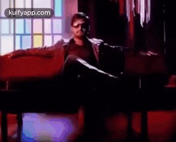 a man wearing sunglasses and a leather jacket is sitting on a couch in front of a window .