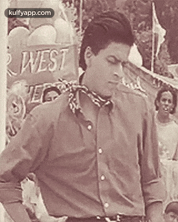 a man in a brown shirt and a scarf around his neck is standing in front of a sign that says west .