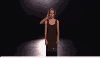 a woman is walking down a runway in a dark room