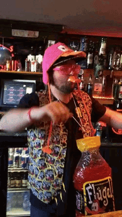 a man wearing a pink hat and sunglasses is pouring a huge bottle of flügel into his mouth