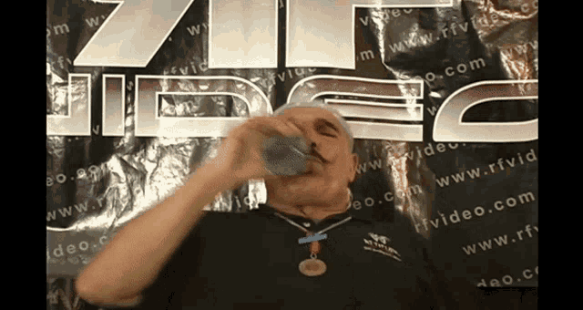 a man is drinking from a cup in front of a sign that says video