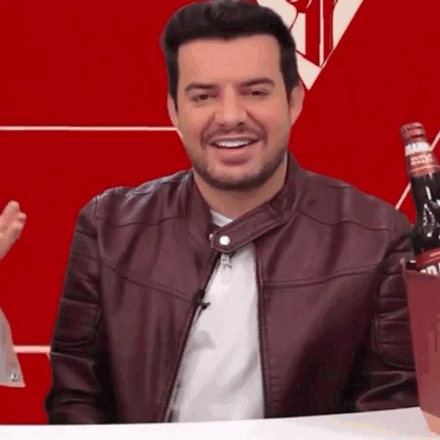 a man in a maroon leather jacket is smiling while holding a bottle of smirnoff
