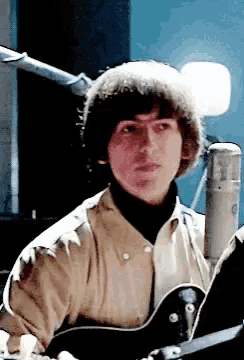 a man is playing a guitar in front of a microphone and looking at the camera