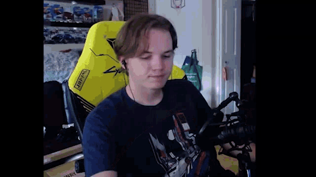 a man in a blue shirt is sitting in a yellow gaming chair with headphones on .