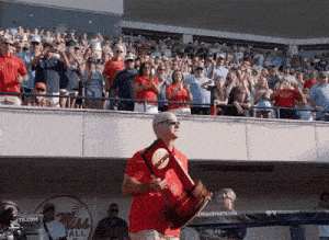 a man in a red shirt is holding a trophy in front of a crowd that is watching a baseball game