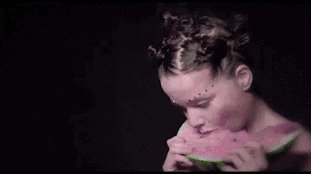 a woman is licking a piece of watermelon in a pink room